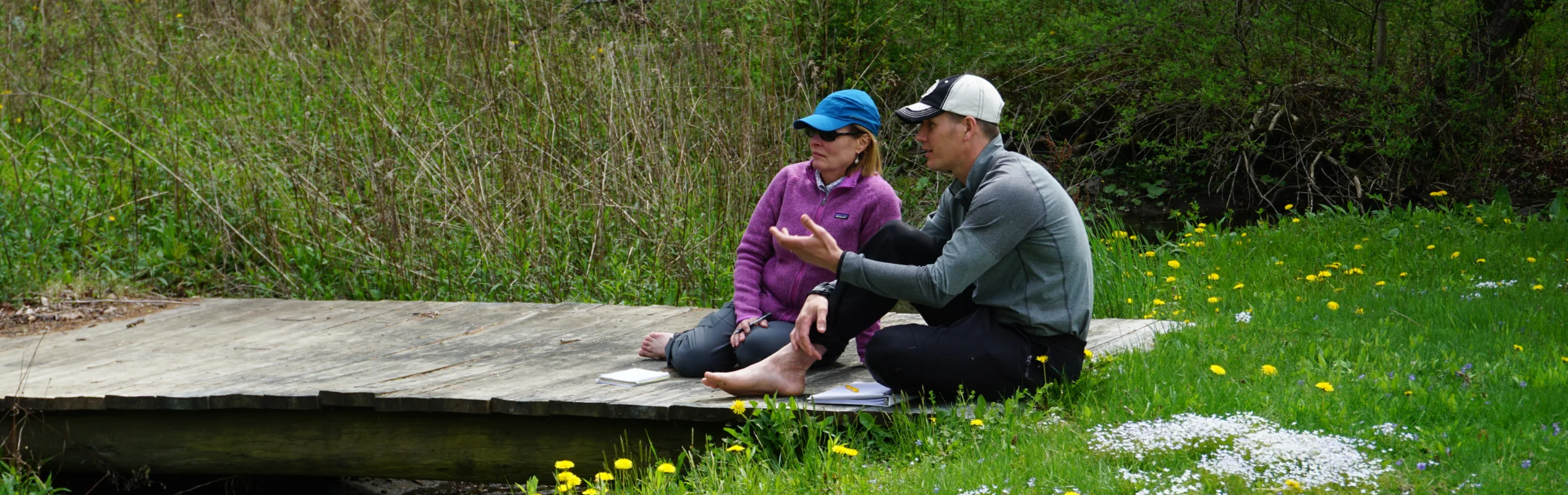 Two people in conversation on a bridge in a wooded landscape