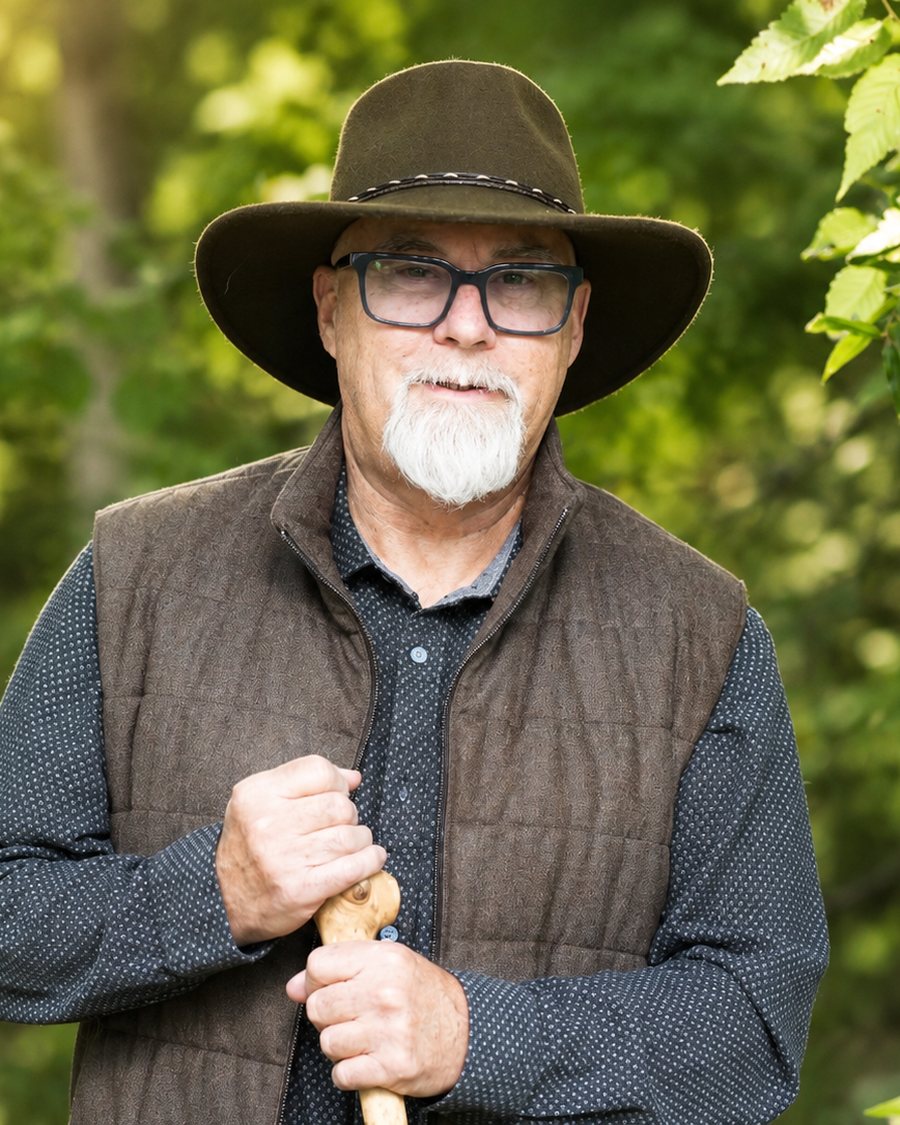 Amos Clifford, founder, standing among trees with hat and walking staff